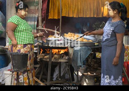 Sagaing/Myanmar-3 ottobre 2019: Due mercanti femminili friggono il cibo in una padella per la vendita al mercato al mattino. Foto Stock