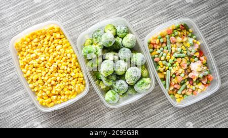 Contenitori in plastica con verdure surgelate su sfondo grigio, vista dall'alto, verdure surgelate diverse sul tavolo, mais germogli di bruxelles fagioli verdi misti Foto Stock