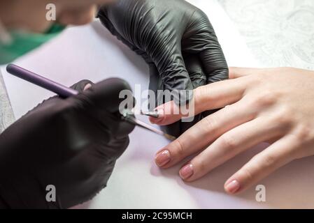 Il processo di creazione di una manicure. Primo piano di una donna in un salone. Estetista mette unghie su un cliente. Foto Stock