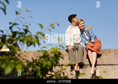 Due giovani fidanzate si abbracciano e si godono l'un l'altro mentre si siede all'aperto Foto Stock