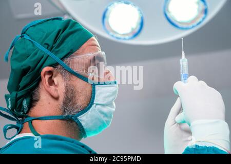 medico professionista che tiene la medicina anestetica generale o la siringa dell'ago del vaccino del farmaco antivirale per il paziente prima dell'intervento chirurgico nella sala operatoria a t Foto Stock