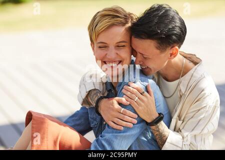 Due giovani lesbiche felici che si siedono all'aperto abbracciando e ridendo Foto Stock