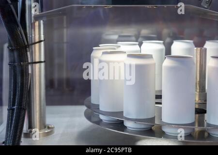 le nuove lattine bianche vuote in alluminio per il processo di produzione di bevande sono in fase di scansione e spostamento in fabbrica sulla macchina a nastro trasportatore nella produzione di bevande. alimenti e b Foto Stock