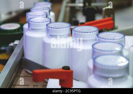 Bottiglia di plastica bianca sulla linea di produzione del nastro alla macchina di riempimento in fabbrica medica. Il fuoco selettivo. Foto Stock