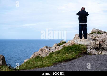 Uomo anziano in piedi sulla scogliera usando binocoli. Foto Stock