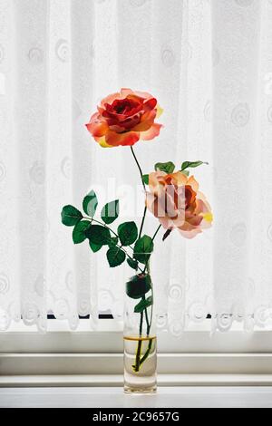 I fiori di plastica sul davanzale incorniciato da tendine Foto stock - Alamy