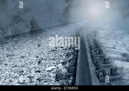 Vecchia ferrovia arrugginita abbandonata in nebbia che scava in lontananza per un giro con luce mistica, immagine monocromatica Foto Stock