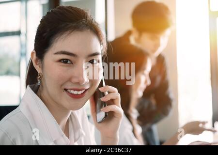 Giovane donna d'affari asiatica bella sorridente affascinante e parlare sul telefono cellulare nella sala riunioni Foto Stock