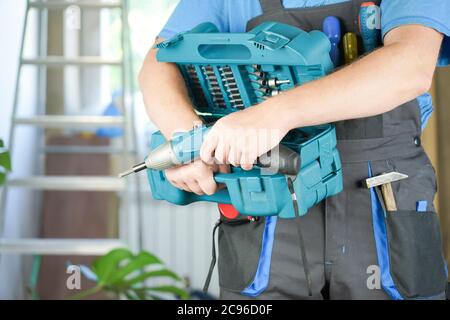 il lavoratore tiene in mano un cacciavite elettrico e una cassetta degli attrezzi Foto Stock