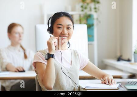 L'operatore del call center asiatico indossa le cuffie sorridendo alla fotocamera e lavora nell'assistenza clienti Foto Stock