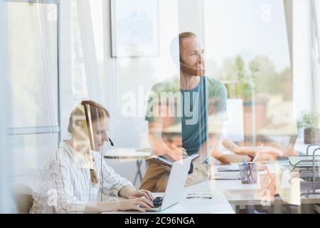 Gruppo di impiegati che lavorano insieme in ufficio dietro la parete di vetro Foto Stock