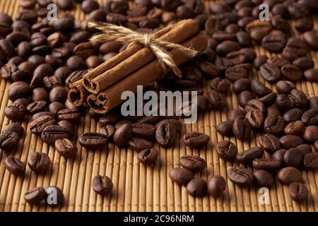 Chicchi di caffè interi marroni arrostiti e bastoncini di cannella legati su un tappetino di bambù Foto Stock