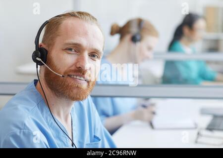 Ritratto di un giovane uomo in cuffia che sorride alla fotocamera mentre lavora in ufficio presso il call center Foto Stock