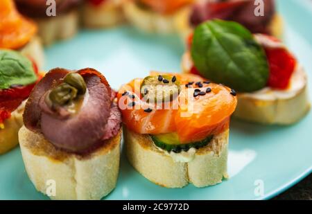 Spuntini antipasto con filetto di pesce al salmone, carne di vitello, capperi su pane servito su piatto blu in close up.Delicious snack preparato con sano naturale Foto Stock