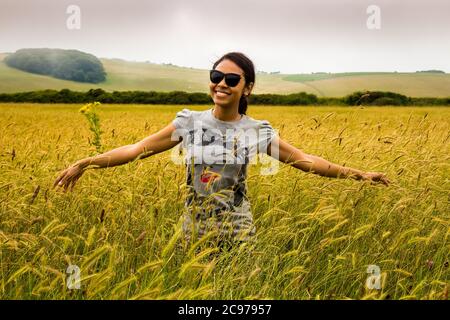 Le donne asiatiche turistiche con occhiali da sole, sorridendo e godendo la lunga erba di un campo inglese, Seven Sisters Country Park, Inghilterra Foto Stock