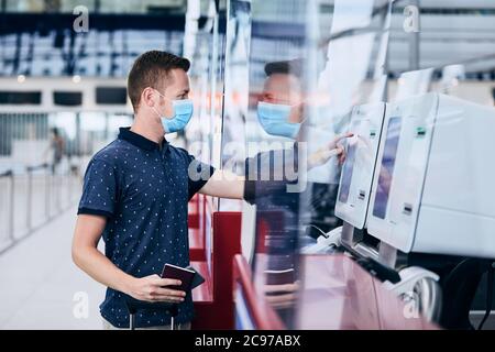 Uomo che indossa la maschera facciale che effettua il check-in self-service all'aeroporto. Temi nuovo normale, coronavirus e protezione personale. Foto Stock