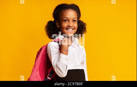 Black Schoolgirl Holding School zaino sorridente in posa in studio Foto Stock