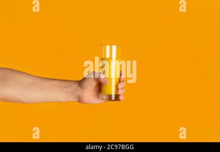 Primo piano di un giovane ragazzo che tiene un bicchiere con succo d'arancia fresco su sfondo colorato, spazio vuoto Foto Stock