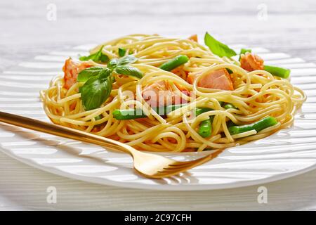 Sana cena al ristorante: Pasta di salmone con spaghetti, fagioli verdi, pesce arrosto e aglio con basilico fresco sulla parte superiore servito su un piatto bianco con forchetta o Foto Stock