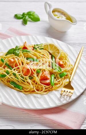 Pasta al salmone con fagioli verdi e salsa al burro all'aglio con basilico fresco e limone cotto con spaghetti italiani e pesce al forno, servito su un bianco Foto Stock