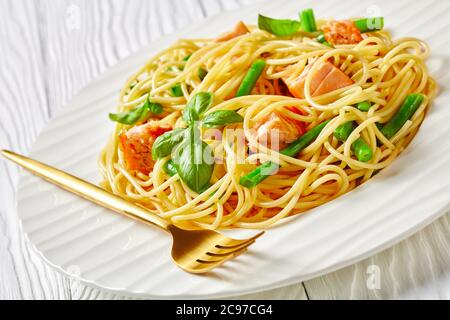 Pasta gourmet di salmone con fagioli verdi e salsa al burro all'aglio con basilico fresco su spaghetti italiani e pesce al forno, servita su un piatto bianco wi Foto Stock