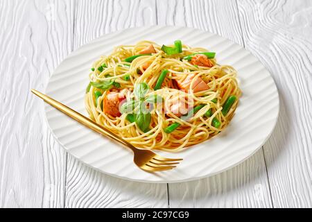 Pasta di salmone selvatico dell'alaska con spaghetti italiani, fagioli verdi e salsa di burro all'aglio con basilico fresco sulla parte superiore, servita su un piatto bianco con forchetta su una merda Foto Stock