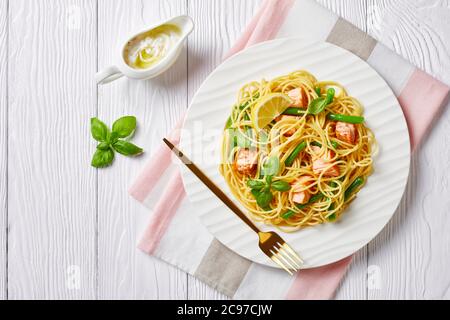 Pasta di pesce di salmone e fagioli verdi, spaghetti italiani, con salsa di burro all'aglio, basilico fresco, limone servito su un piatto bianco con forchetta su un bianco Foto Stock