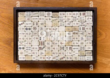 In cima a un gioco di mahjong vintage con le tessere ben memorizzate con la scritta cinese in una tavola nera posta al centro su un tavolo di legno Foto Stock