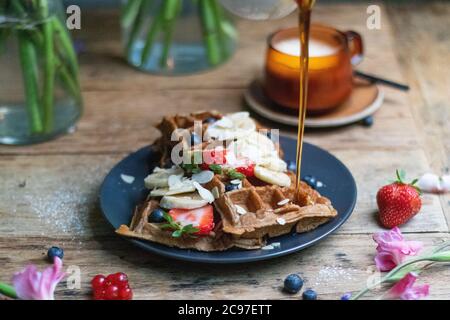Primo piano di cialde con banane fresche e fragole con miele che si versa su ti Foto Stock