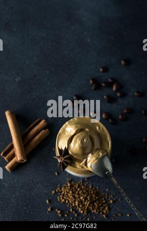 Caffè Dalgona in una tazza trasparente su sfondo scuro. Bevanda sudcoreana con caffè istantaneo montato, zucchero e latte. Foto Stock