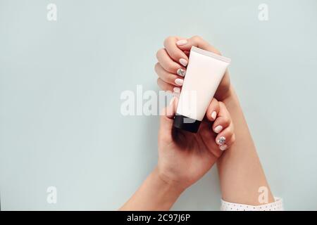 Vista dall'alto di una donna anonima con mani curate che mostra un tubo bianco di crema su sfondo azzurro Foto Stock