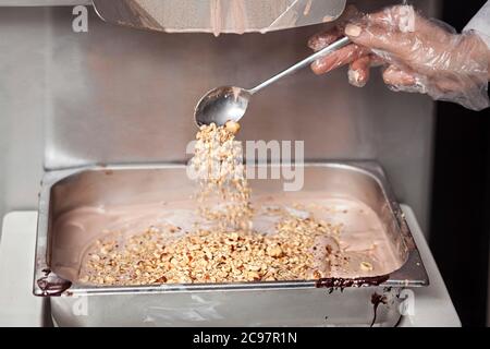 Preparazione del gelato - versare noci nella teglia d'acciaio con gelato nella piccola produzione - primo piano Foto Stock