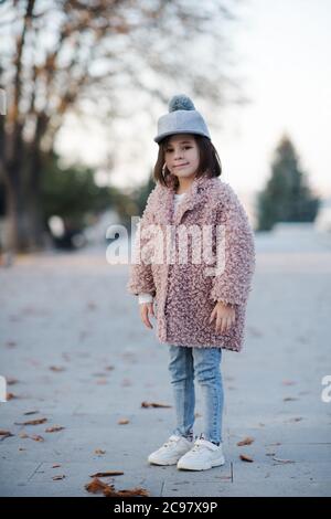 Bella ragazzina di 5-6 anni che indossa cappotto invernale e cappello elegante in posa in parco all'aperto. Stagione autunnale. Infanzia. Felicità. Foto Stock