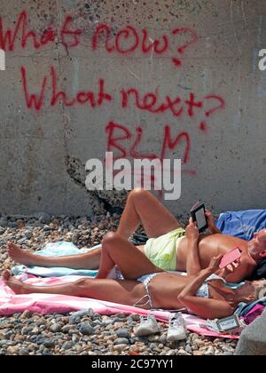 Prendere il sole sulla spiaggia di Brighton da alcuni graffiti BLM Foto Stock