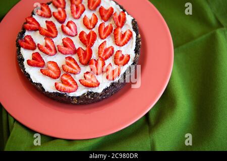 Una cheesecake alla fragola decorata con fragole a forma di cuore giace su un piatto color corallo e si erge su un tovagliolo verde. Illustrazione di un cheesec Foto Stock