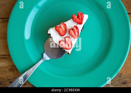 Un pezzo di cheesecake alla fragola decorato con fragole a forma di cuore giace su un piatto color menta e si erge su un tovagliolo a scacchi. Vista da abo Foto Stock