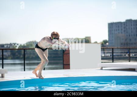 Uomo in occhiali da bagno che spinge fuori dal bordo della piscina Foto Stock