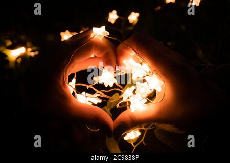 Luce a LED a forma di stella e mani a forma di cuore d'amore con sfondo scuro. Festa di San Valentino. Foto Stock