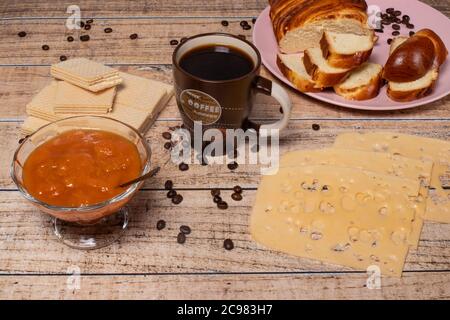 L'idea di una deliziosa colazione per tutta la famiglia. Panino di vimini, formaggio, marmellata di albicocche, waffle e caffè nero aromatico. Foto Stock