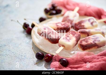 Panna fresca e ciliegia pop-icles fatti in casa posto su piastra di ceramica bianca con frutta e tessuto Foto Stock