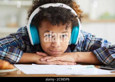 Primo piano di uno studente africano con capelli ricci in cuffie guardando la fotocamera mentre si siede al tavolo e si studia Foto Stock