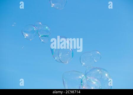 Bolle surreali che galleggiano un cielo blu chiaro in una giornata di sole e scintillanti nel sole brillano. Creato da un Bubbleologo in occasione di un evento all'aperto. UK (120) Foto Stock