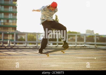 Skateboarder fare un trucco in città strada sotto il sole d'estate. Giovane uomo in sneakers e berretto a cavallo e skateboard sull'asfalto. Concetto di attività di svago, sport, estremo, hobby e movimento. Foto Stock