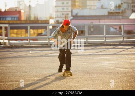 Skateboarder fare un trucco in città strada sotto il sole d'estate. Giovane uomo in sneakers e berretto a cavallo e skateboard sull'asfalto. Concetto di attività di svago, sport, estremo, hobby e movimento. Foto Stock