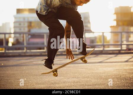 Skateboarder fare un trucco in città strada sotto il sole d'estate. Giovane uomo in sneakers e berretto a cavallo e skateboard sull'asfalto. Concetto di attività di svago, sport, estremo, hobby e movimento. Foto Stock