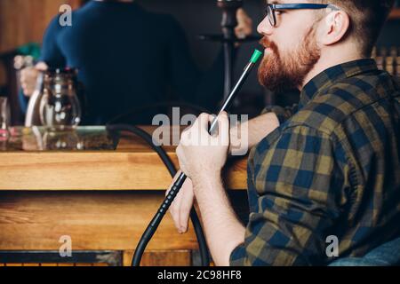 Il tipo pensivo dai capelli rossi fuma. Vapore dal gancio.primo piano vista laterale foto. Tempo libero. Hobby. Tempo libero. Tempo libero Foto Stock