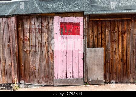 Decrepit porta garage in legno con profilo porta di accesso rosa dipinto a Southend on Sea, Essex, UK. Area urbana. Struttura in decadimento Foto Stock