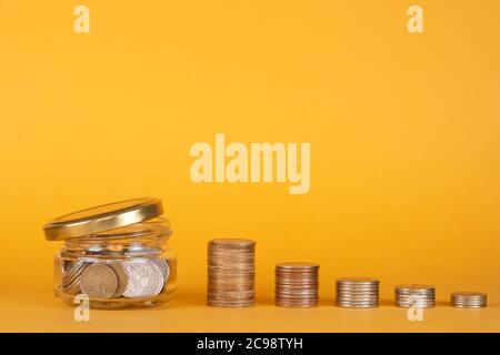 Vasetto di vetro con monete su sfondo giallo, spazio di copia per il testo Foto Stock
