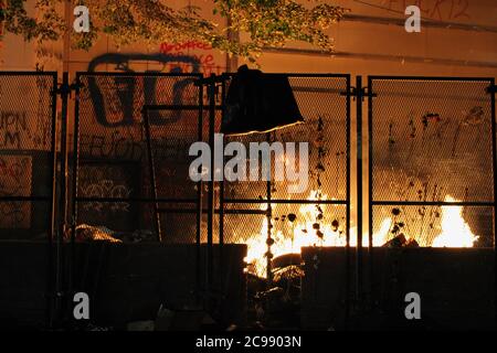 28 luglio 2020, Portland, Oregon, U.S: Proteste di Portland: La fazione anarchica dei manifestanti ripulisce il parco di fronte al Centro di Giustizia e gettano la spazzatura sopra la recinzione che i Feds hanno messo su durante il fine settimana per tenere il pubblico fuori della proprietà che ritengono appartiene alla gente e sta occupandosi illegalmente Agenti federali fascisti e razzisti inviati da un presidente Trump che sta violando i diritti costituzionali. Qualcuno allora ha regolato la spazzatura sul fuoco per disegnare i Feds fuori per confrontarli. I Feds sono venuti fuori per metterlo fuori, poi ritordati dalla lacrima che gassava il quartiere, spra Foto Stock