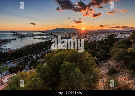 Tramonto sui tetti della città di Malaga. Costa spagnola in Andalusia con raggi solari e nuvole. Vista della città sulla Costa del Sol da un'altura p Foto Stock